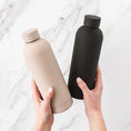Load image into Gallery viewer, a person holding a black and a beige bottle

