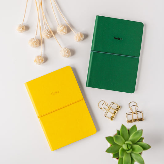 a green notebook, a pair of earrings, and a plant on a white surface