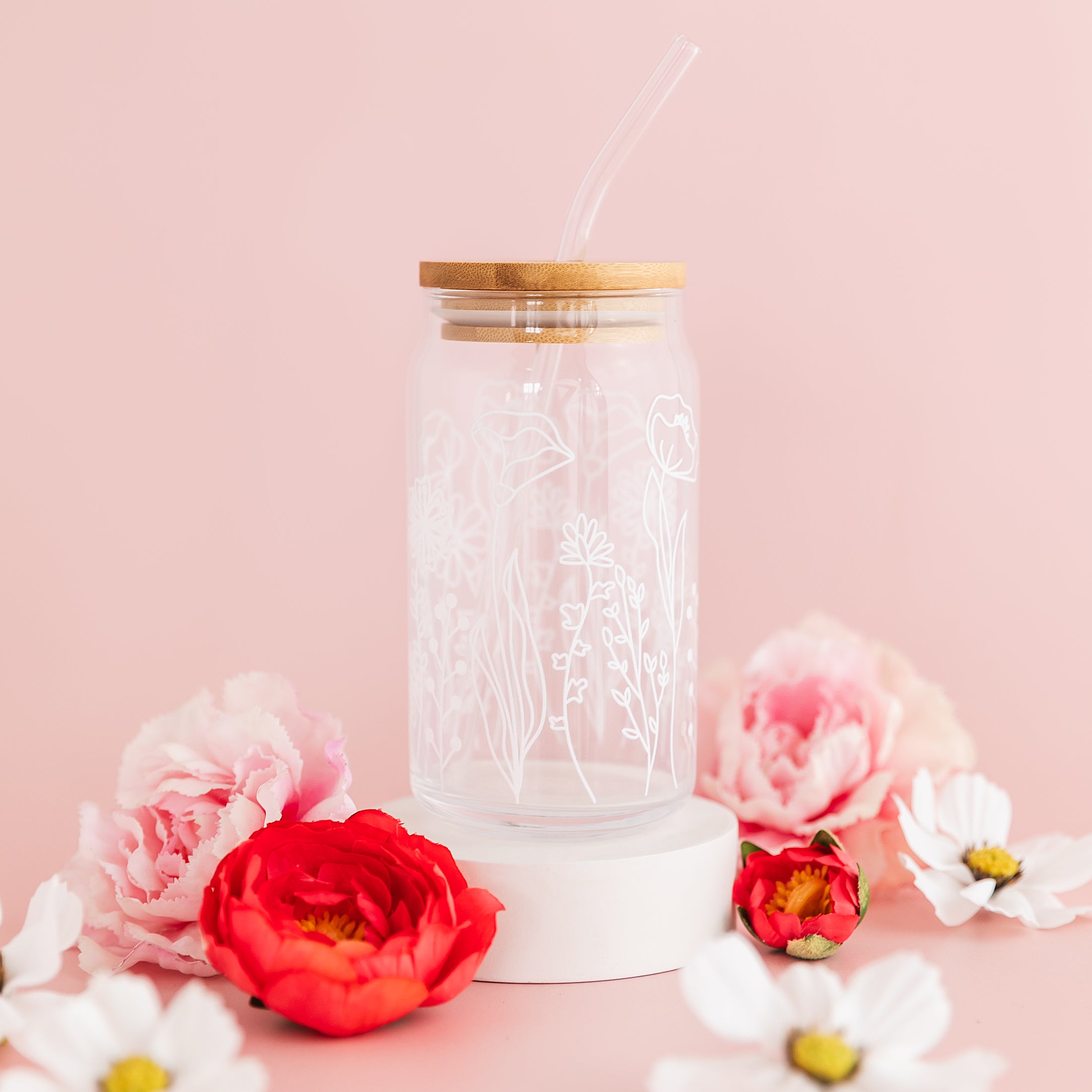 a glass jar with a straw and a flower on a pink background
