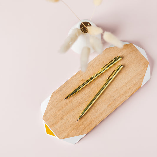 a wooden cutting board topped with two gold colored pens