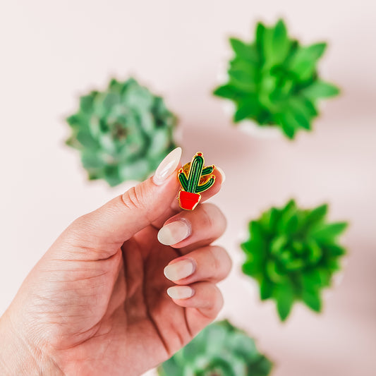 a woman's hand holding a pin with a plant on it